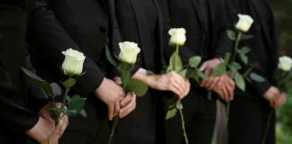 People in black holding white roses in a line.