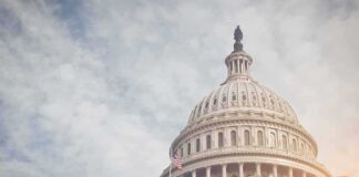 Capitol dome with American flag, under cloudy sky.