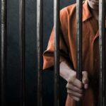 Person in orange shirt behind jail bars.