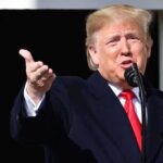 Person speaking into a microphone, gesturing with hand.