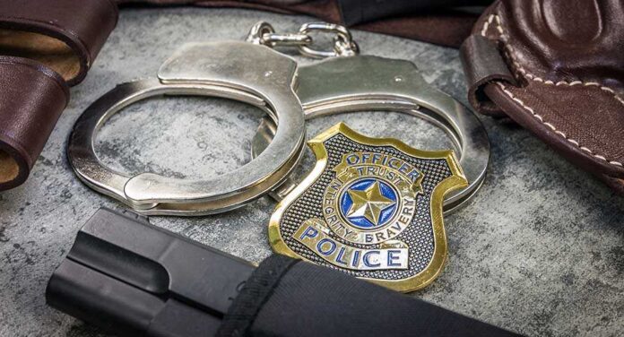 1939544200 featured image Handcuffs, officer badge, and firearm on textured surface.