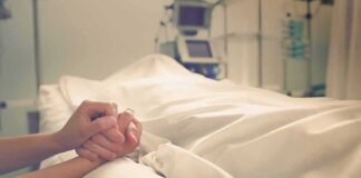 Person holding another's hand in a hospital bed.