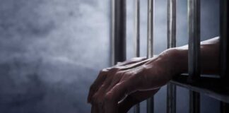 Hands gripping prison cell bars.