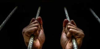 Hands in handcuffs gripping jail bars.