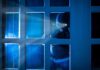 Masked figure peering through glass door at night