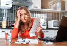 Woman looking stressed holding bills in kitchen