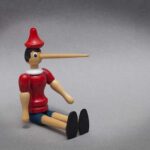 Wooden puppet with long nose sitting on grey background