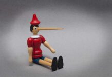 Wooden puppet with long nose sitting on grey background