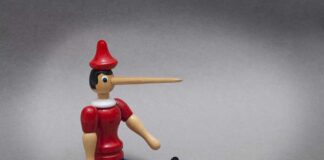 Wooden puppet with long nose sitting on grey background