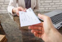 Hands exchanging a check near a laptop