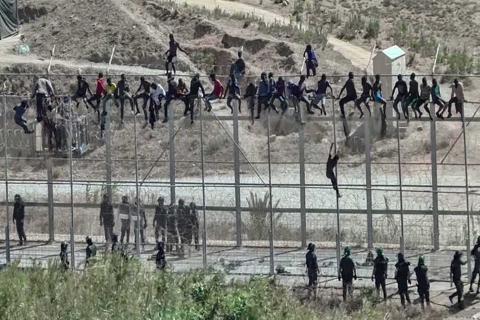 1300621204 featured image People climbing fence watched by security personnel below