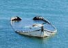 Half submerged weathered abandoned boat floating on calm water
