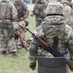 Soldiers in camouflage gear gathered on grass field