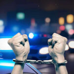 Handcuffed hands raisedpolice cars with lights on