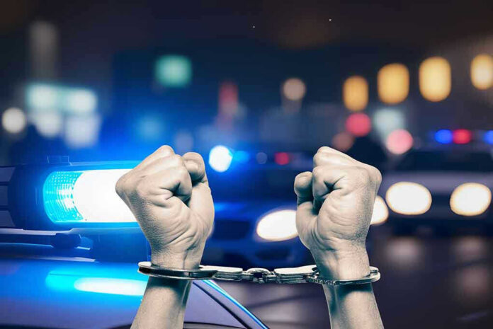 2348949967 Handcuffed hands raisedpolice cars with lights on