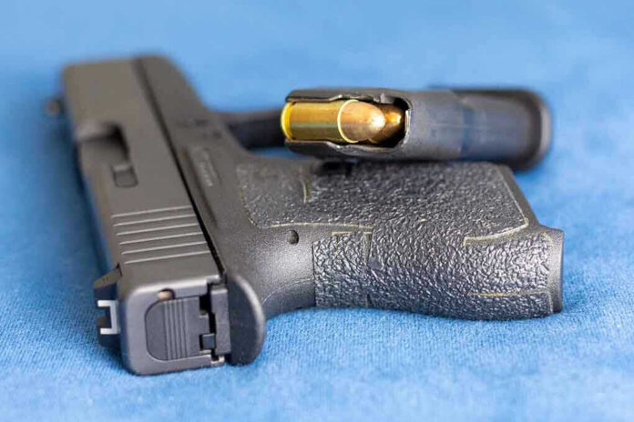 2159542825 Handgun on blue fabric with visible bullet cartridge.