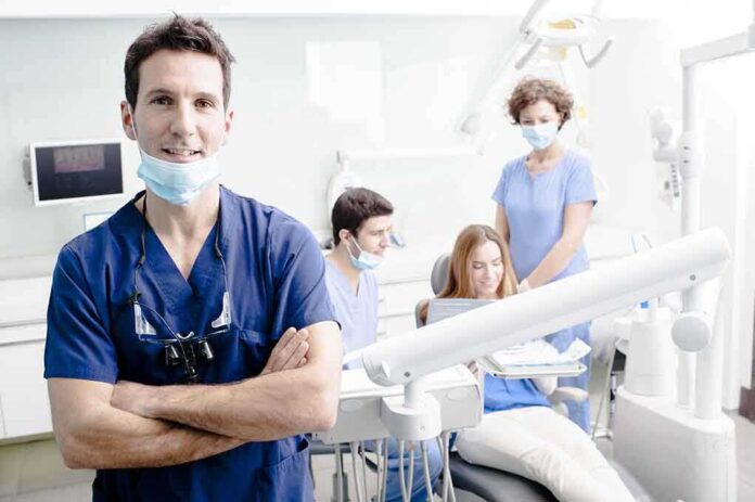 shutterstock_138700625.jpg A dentist smiling in a dental office with a team assisting a patient