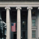 US Treasury Department building with statue and flag.
