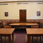 Senate Hearing TURNS NASTY – Personal Blows Traded! Empty courtroom with wooden tables, chairs, and a door.
