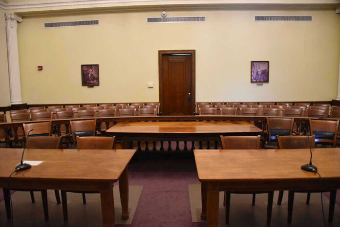 Empty courtroom with wooden tables, chairs, and a door.