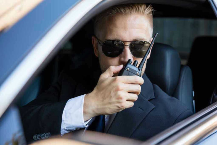 Man in suit using walkie-talkie in car.