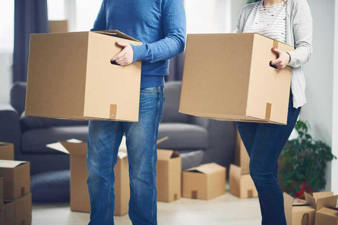 Two people carrying cardboard boxes indoors.