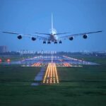 An airplane approaching the runway at night with landing lights illuminated