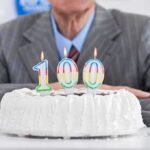 A man in a suit sitting in front of a birthday cake with 100 candles