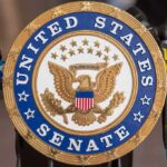 Official seal of the United States Senate with microphones in the background