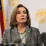 A female politician speaking at a press conference with an American flag in the background