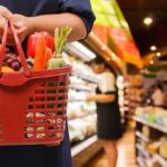 Person holding a basket filled with colorful vegetables in a supermarket
