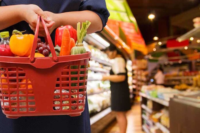 Person holding a basket filled with colorful vegetables in a supermarket