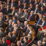 Audience of officials sitting and reading documents in auditorium.