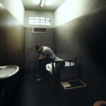 A person sitting in a dimly lit prison cell, appearing contemplative and distressed