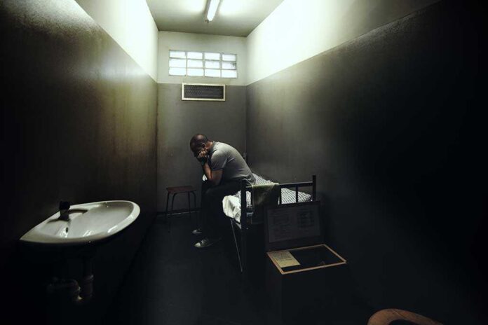 A person sitting in a dimly lit prison cell, appearing contemplative and distressed