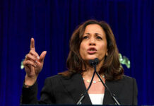 Woman speaking passionately at a podium, gesturing upward.