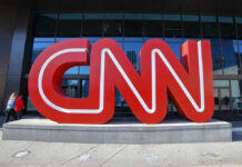 Noem Embarrasses CNN Host on Air – EXPLOSIVE Clash! Large red CNN sign outside building entrance.