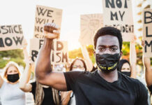 Protester raises fist, wears mask, signs in background.