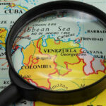 Magnifying glass focusing on Venezuela and Colombia on map.