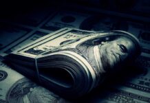 A rolled stack of hundred-dollar bills on a background of more banknotes