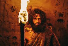 A prehistoric man holding a torch in front of cave paintings