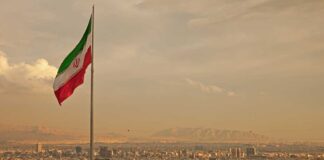 Iranian flag waving over a city skyline with mountains in the background