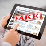Person holding a tablet displaying a news website with a 'FAKE' stamp