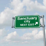 Green road sign saying sanctuary city next exit