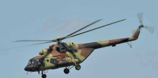 Camouflage military helicopter in flight against blue sky.