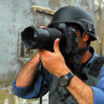 Person in helmet taking photos with a large camera.