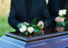 People placing white roses on a casket.