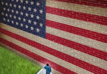 A man in a suit standing in front of a large American flag painted on a wall