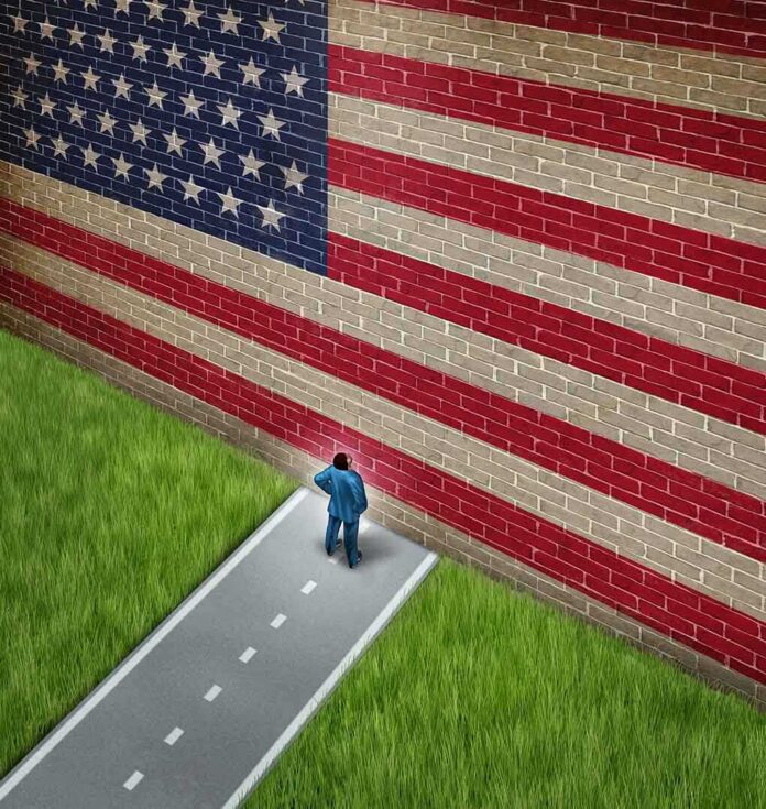 A man in a suit standing in front of a large American flag painted on a wall