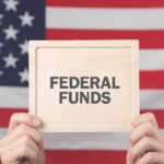 Person holding a sign that reads 'FEDERAL FUNDS' in front of an American flag